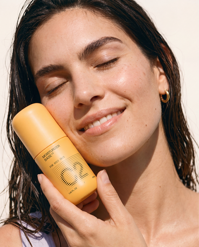 Woman with glowing skin holding a yellow Moisturizer Base bottle.